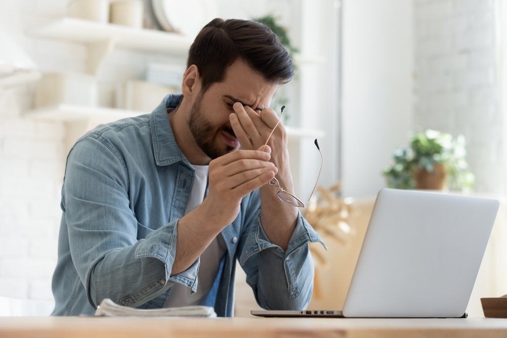 A man experienced discomfort from dry eyes and rubs his eyes by working on the laptop